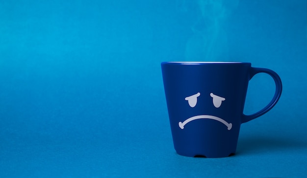 Photo blue coffee cup with a sad face drawn. blue monday concept