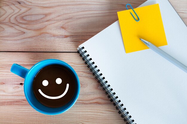 A blue coffee cup with a yellow notepad and a smile on it.