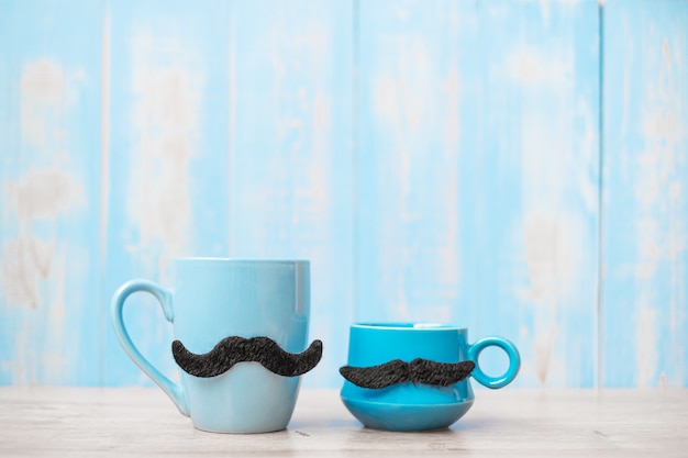 Синие кофейные чашки с черными усами на фоне деревянного стола утром. День отца и концепция международного мужского дня
