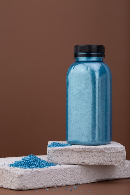 Photo blue colored bath salt in bottle on brown backhround and concrete podium with copy space