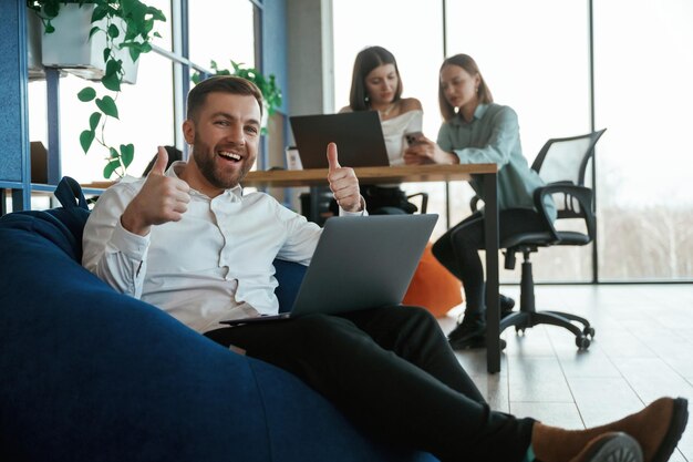 Photo in the blue colored bean bag with laptop people are working in the office