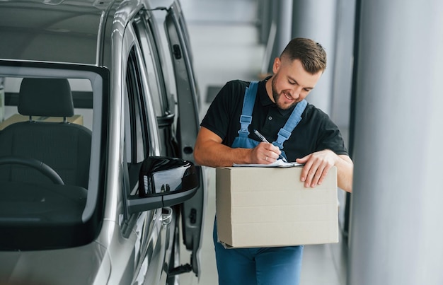 In blue colored clothes Delivery man in uniform is indoors with car and with order