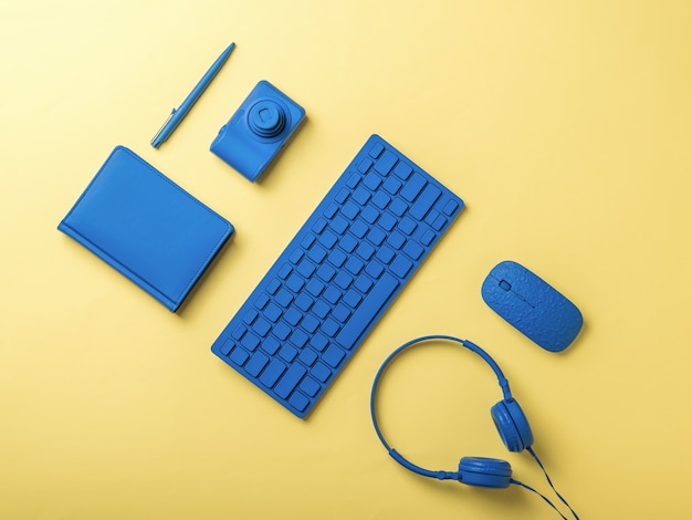 黄色の背景に青いコンピューターと文房具のアクセサリー。ビジネスやフリーランス向けのスタイリッシュなアクセサリー。フラットレイ。