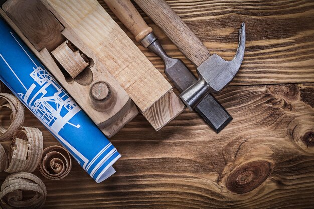 Blue construction plan shaving plane claw hammer chisel wooden studs shavings on wood board.