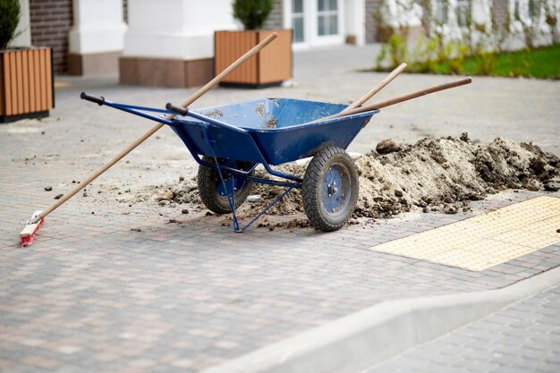 写真 通りにシャベルが付いた青い建設用手押し車青い鉄の手押し車と石畳