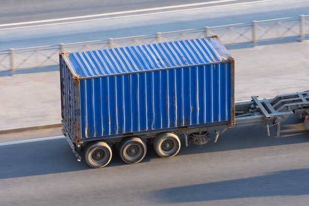 Blue container trailer driving on a highway at high speed.