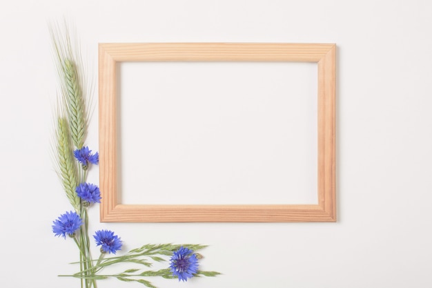 Blue cornflowers and cereals with wooden frame on white surface