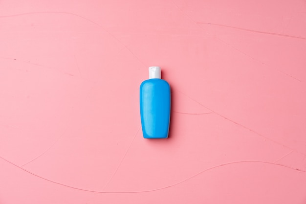 Синяя косметическая бутылка на текстурированном розовом фоне