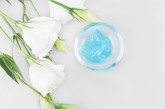 Blue cosmetic face mask standing on white background and flowers