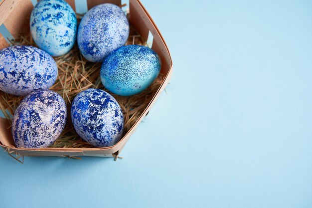 blue cosmos chicken eggs lie in round wooden basket which stands on a blue background.