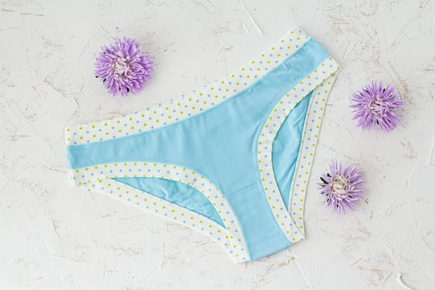 Blue cotton panties with flower buds on the white structured background. Woman underwear set. Top view.