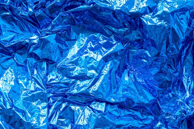 Blue crumpled creased iridescent metal foil texture abstract colored background shiny monochrome