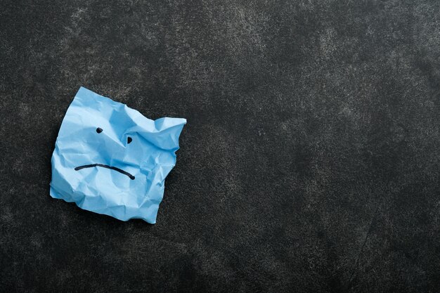 Blue crumpled sticky notes blank with drawing sad face on black background with copy space ready for your message Blue Monday and mental health concept idea Flat lay copy space on black background