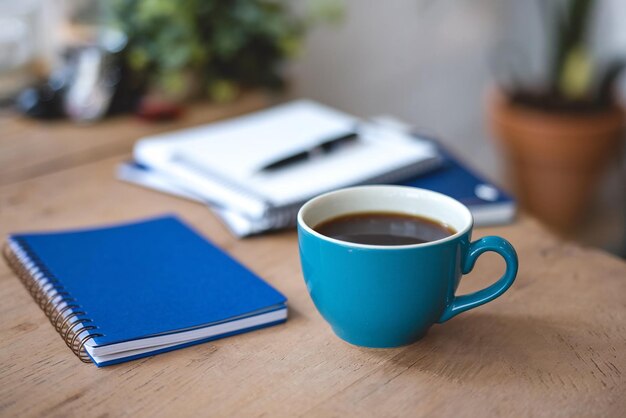 a blue cup of coffee sits on a table next to a notebook