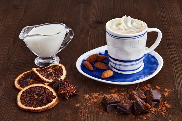 Blue cup of coffee with cream, chocolate, milk and spices on a dark wooden table