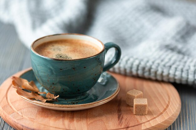 Blue cup withcoffee knitted sweater autumn leaves on wooden background cozy morning