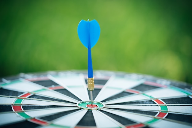 Photo blue dart arrows hitting in the target center of dartboard with green nature background.