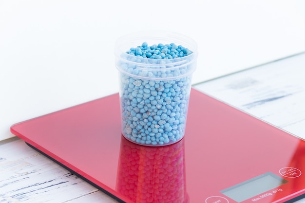 Blue different shape chemical fertilizer granules in glass on red scale