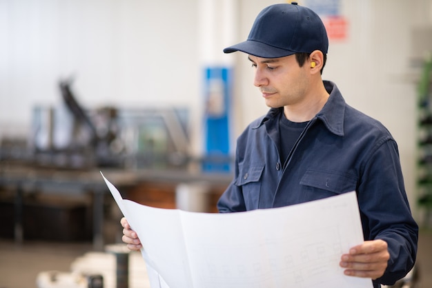 Blue dressed engineer reading a bluepring drawing in an industrial facility