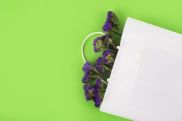 Blue, dried flowers in white paper bag on the green background.. Close up. Top view, copy space