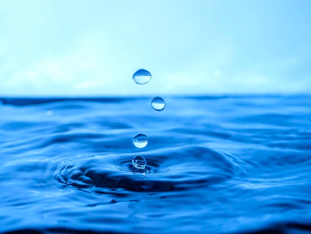Голубая капля капает в воду и создает брызги различной формы, волны создаются через воду, концепция жидкого всплеска, субстанция окрашена в синий цвет