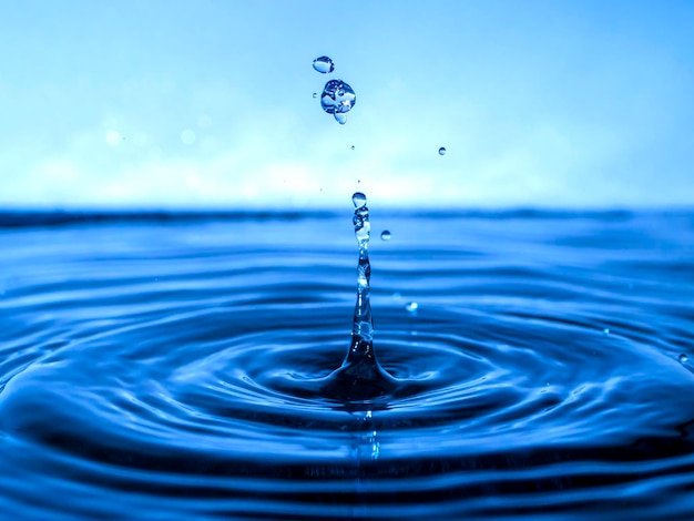 A blue drop drips into the water and creates splashes of various shapes, waves are created through the water, the concept of a liquid splash, a substance painted in blue color