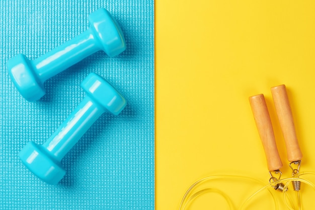 blue dumbbells and jump rope on a blue and yellow background