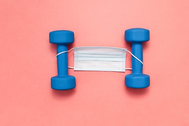 Blue dumbbells on pink background with medical mask