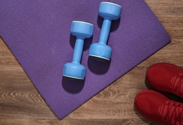 Blue dumbbells, red sport shoes and fitness mat on wooden floor. Workout concept.