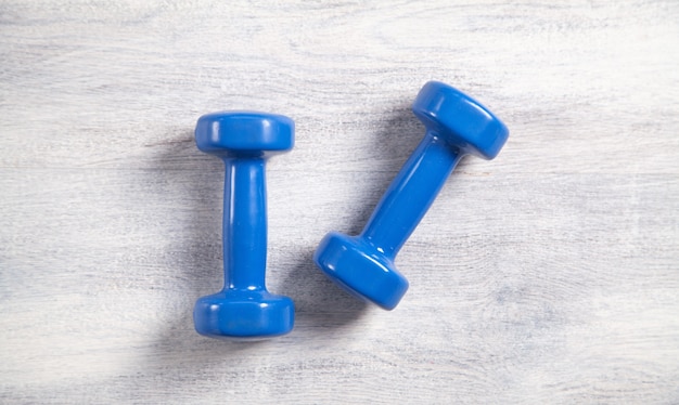 Blue dumbbells on white wooden background.