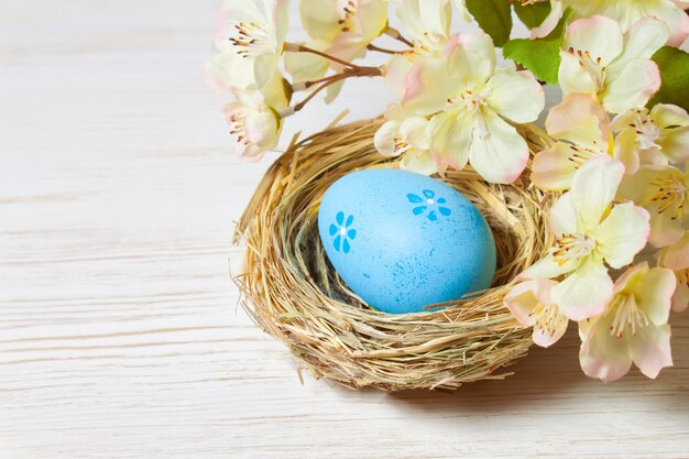 Синее пасхальное яйцо в соломенном гнезде и ветке