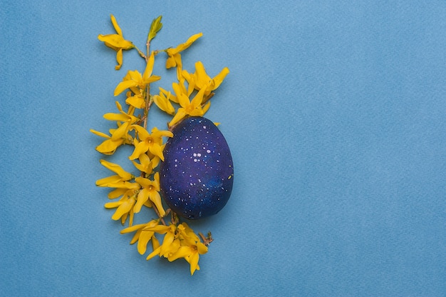 Foto uovo di pasqua blu con fiori gialli su sfondo blu.