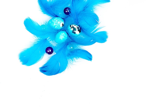 Blue easter eggs and small fluffy blue feathers randomly\
scattered on white table