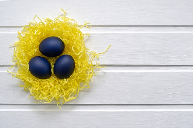 Blue easter eggs in a yellow nest on a white wooden