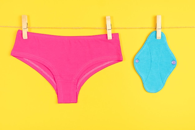 Blue eco reusable menstrual pads and pink underpants on washing line yellow background Health care and zerowaste no plastic ecofriendly concept