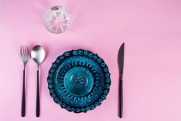Синяя пустая тарелка и стакан с серебряной вилкой, ложкой и ножом
