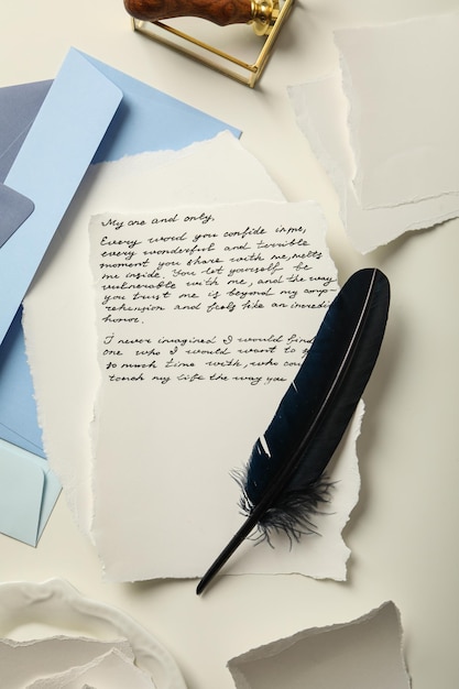Foto buste blu fogli di carta piuma di uccello e lettera con testo su sfondo bianco vista dall'alto