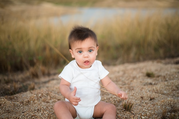 Blue-eyed baby sitting on the sand floor near the grass