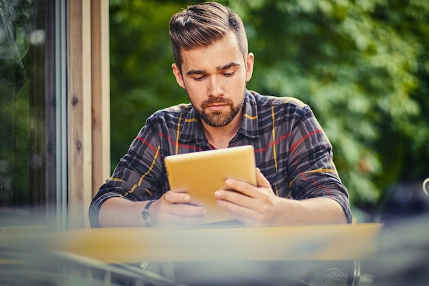 通りのカフェでタブレットPCを使用して青い目のひげを生やした男性。