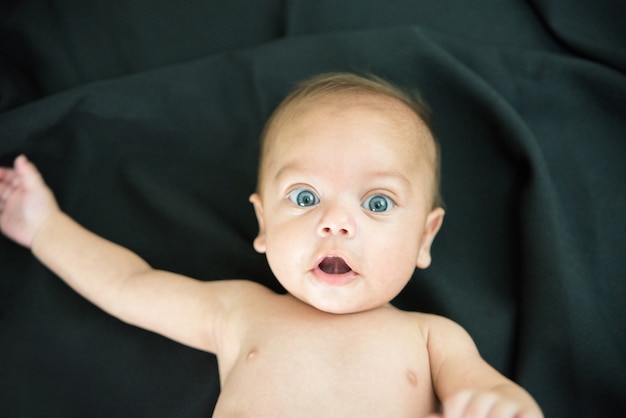 Blue eyed naked baby lying on black fabric