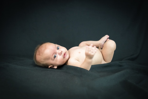 Blue eyed naked baby lying on black fabric