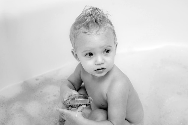 카메라를 보고 웃고 있는 작고 귀여운 귀여운 블론을 목욕하는 양동이에 있는 파란 눈 아이