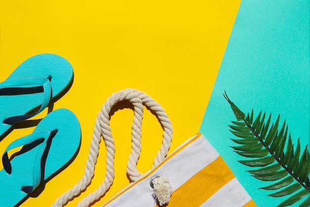 Blue flip flops, beach bag and palm leaf on yellow and turquoise background