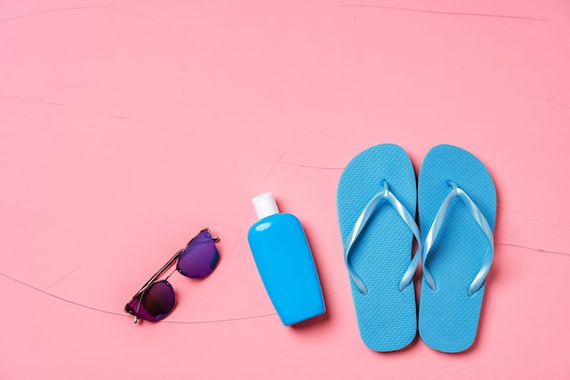 Blue flip-flops with sunscreen and sunglasses on pink, flat lay