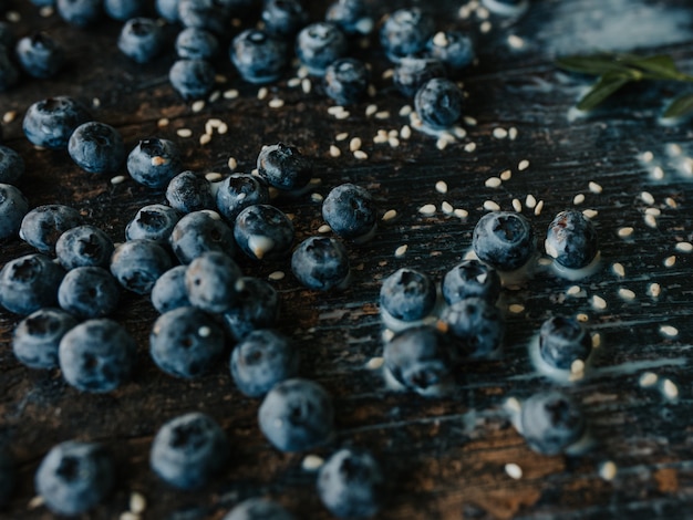 blue fresh blueberries are scattered on an old brown wooden cracked table. sesame seeds