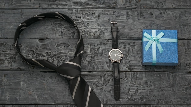 A blue gift box, a tie and a watch on a wooden background.