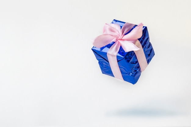 Blue gift box with pink ribbon flying on white background.