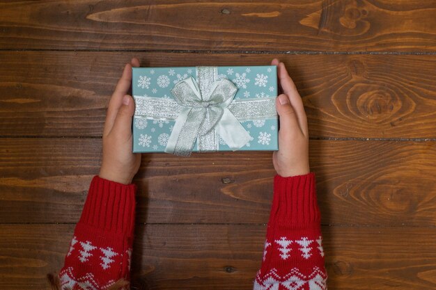 Blue gift in kids hands on dark wooden background