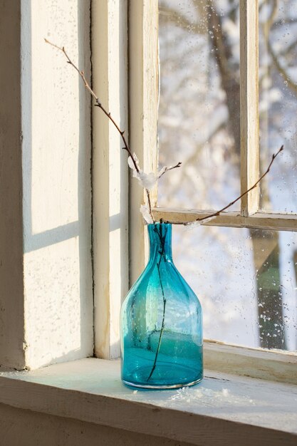 Blue glass bottle with branch on old winter window