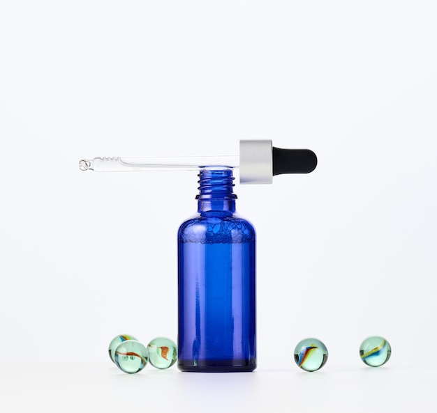白い背景の上のピペットと青いガラス瓶。化粧品液体製品、広告、プロモーションのテンプレート